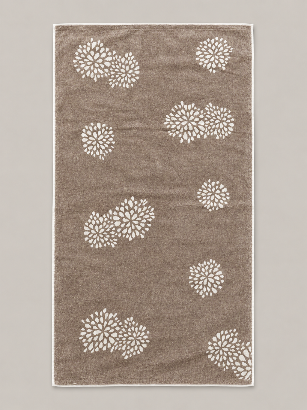 Brown bath towel with repeated white floral motifs measuring 72 x 136 cm