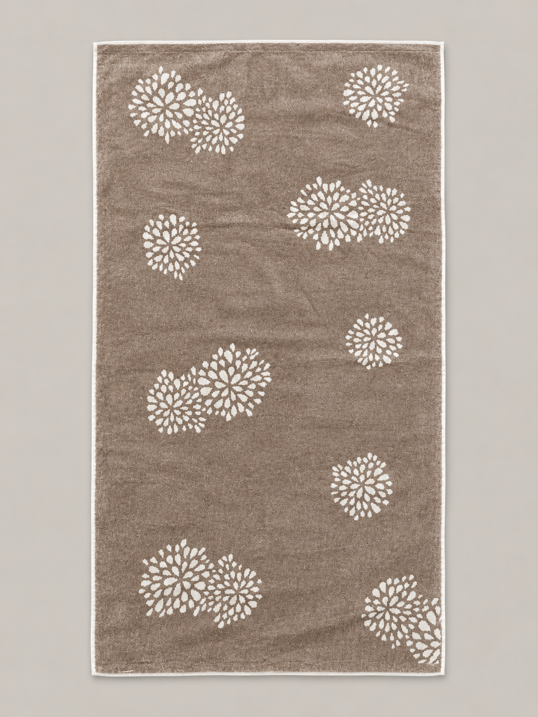 Brown bath towel with repeated white floral motifs measuring 72 x 136 cm