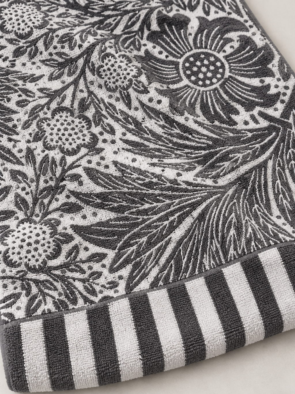 Close-up of the botanical floral pattern and striped border on a charcoal gray and white bath towel