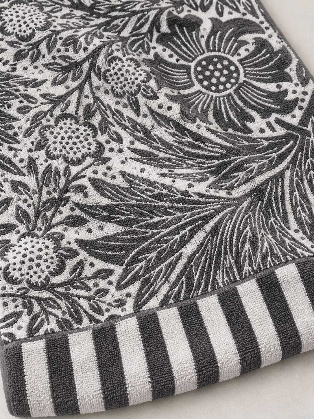 Close-up of the botanical floral pattern and striped border on a charcoal gray and white bath towel