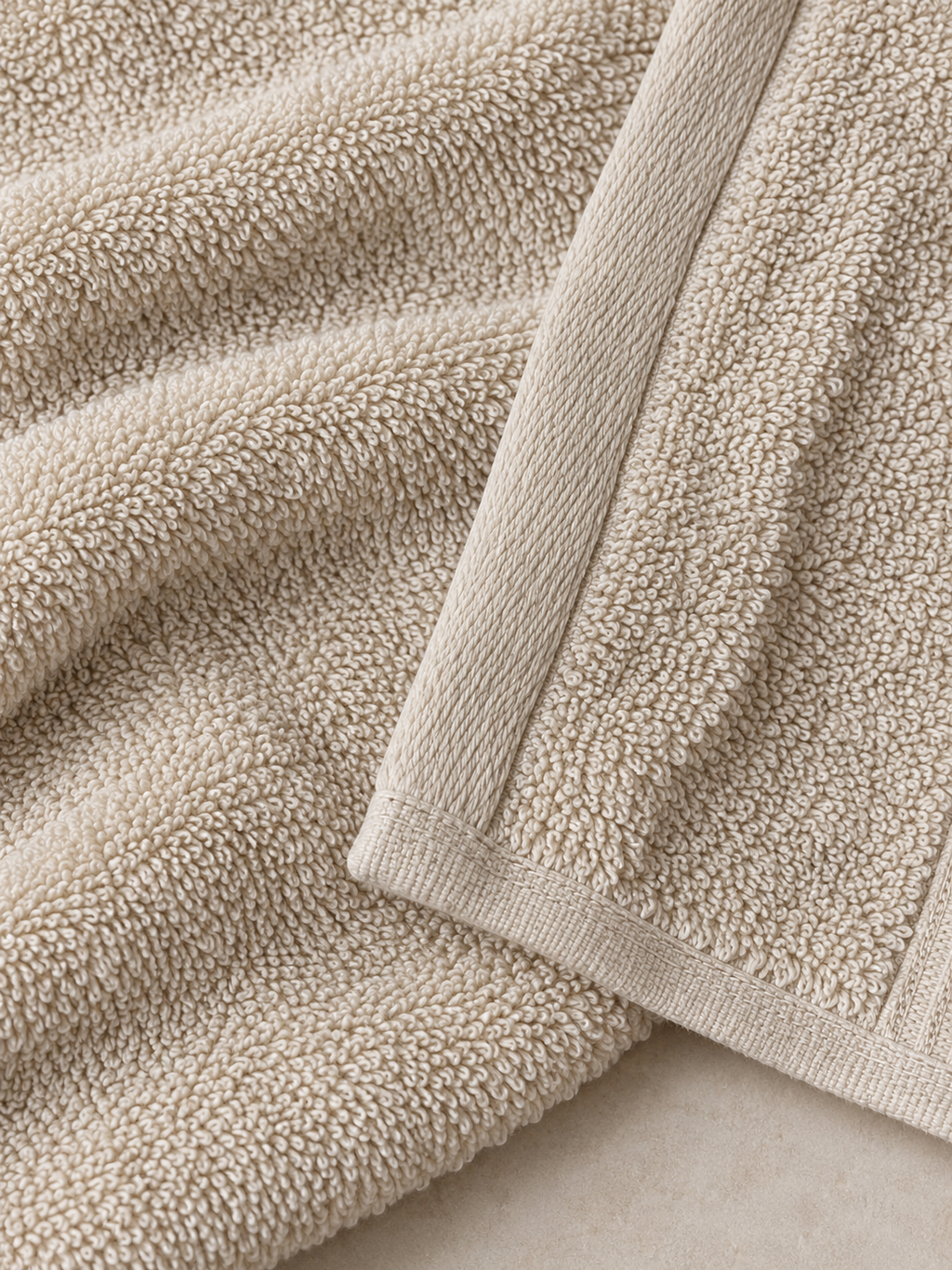 Close-up of the dense looped terry texture and finished edge of a cream bath towel