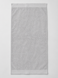 Light gray terry towel with broad woven end borders measuring 75 x 148 cm on a light gray studio background