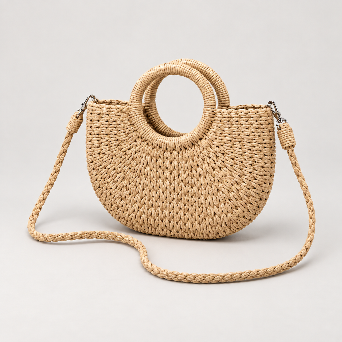 Natural tan woven crossbody bag with round ring handles on a light gray studio background